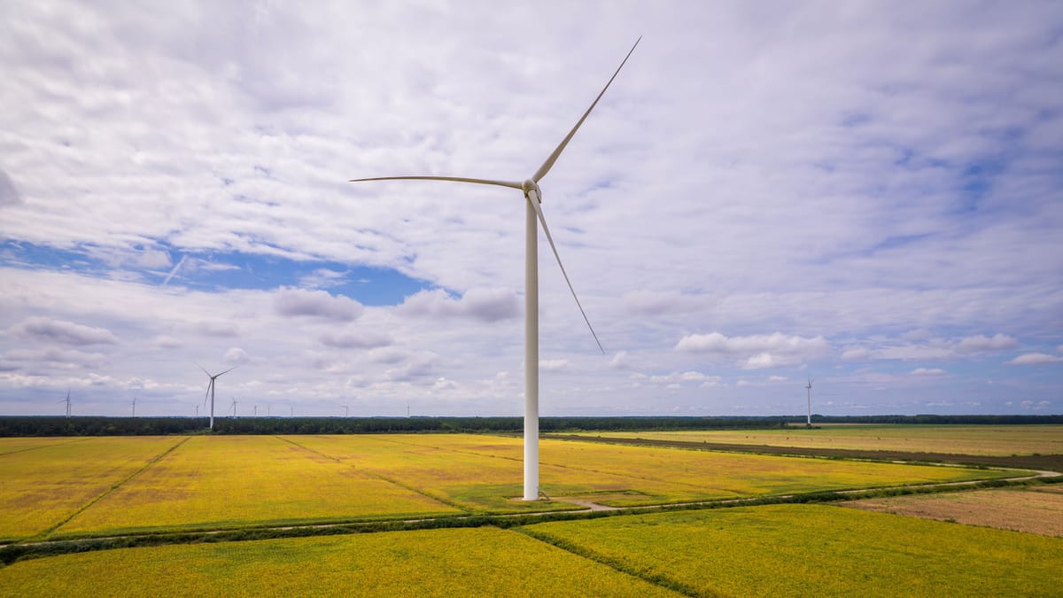 Aerial view of a wind turbine standing among farm fields, representing remote infrastructure operating environments for commercial drone teams.