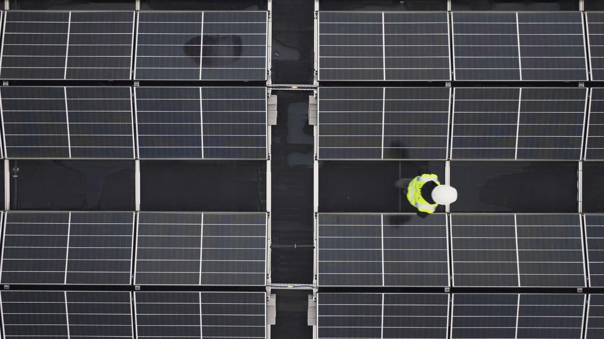 Aerial view of a worker in hi-vis safety gear inspecting solar panels.