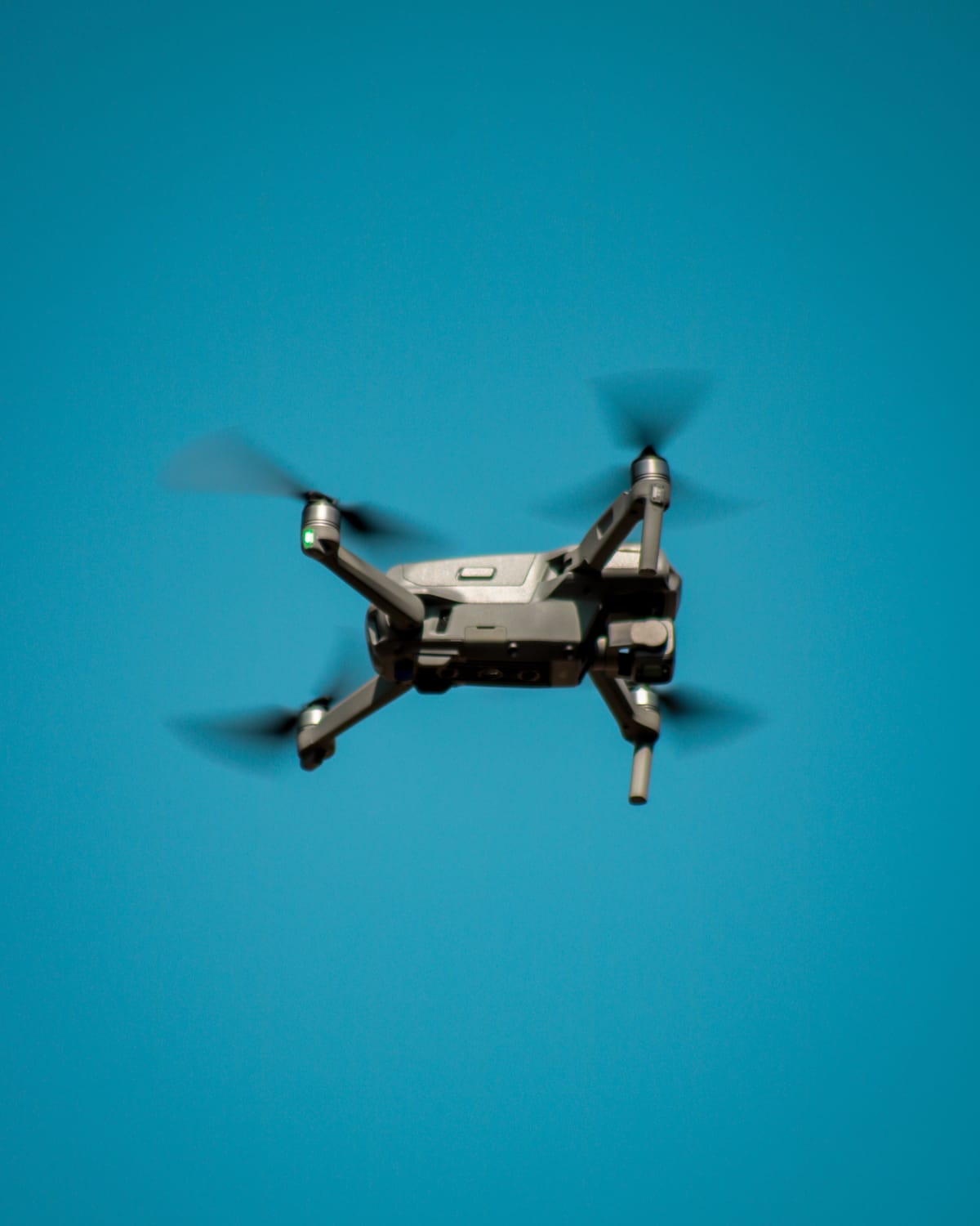 Drone flying in clear blue sky, low-angle view from below.