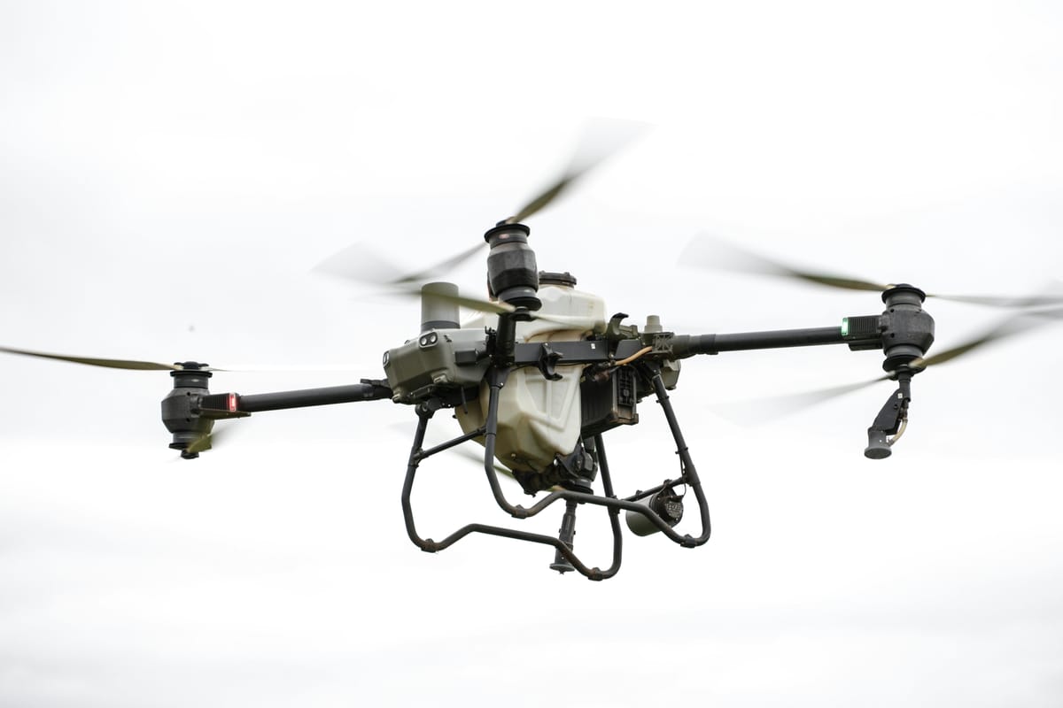 Specialized agricultural crop-spraying drone in flight over a green field.