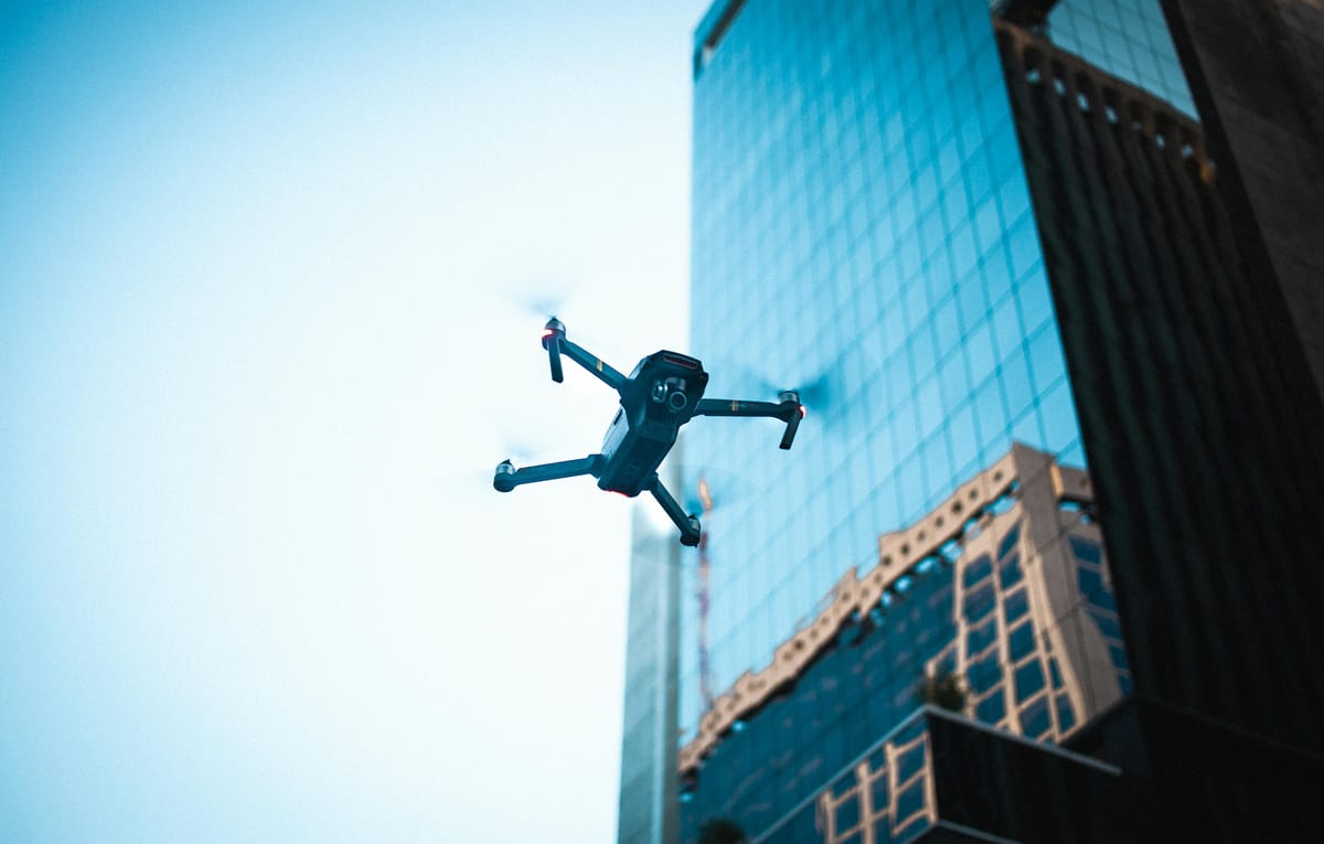 Drone hovering near a modern glass and steel skyscraper against a clear sky.