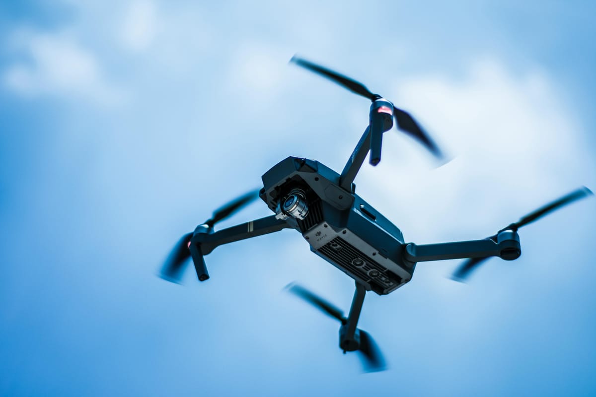 Small drone hovering against a clear blue sky.
