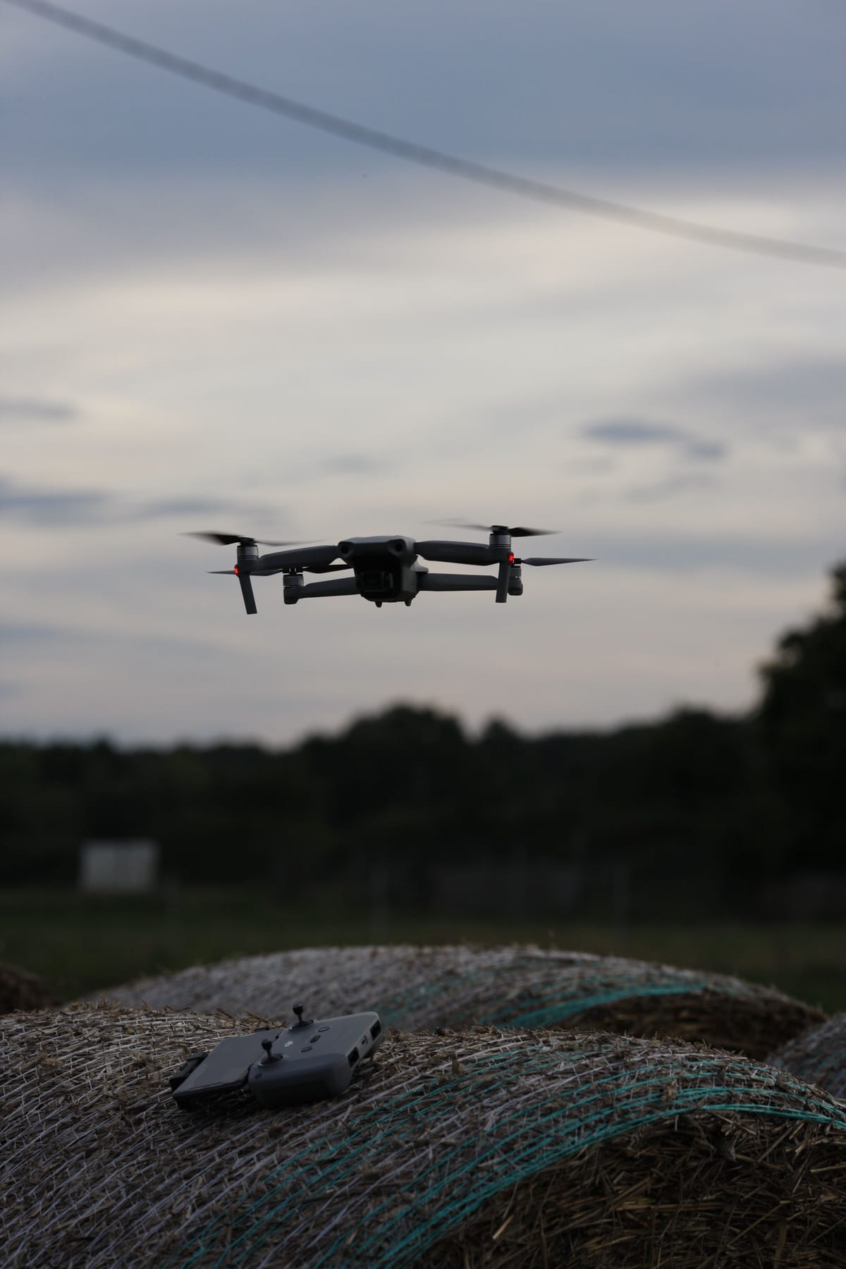 Drone hovering above a remote controller in a rural field at dusk.