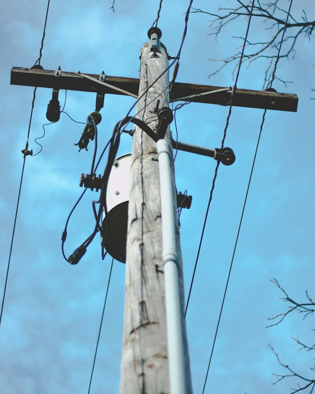 A wooden utility pole with crossarm, insulators, cables and conduit against a blue sky.
