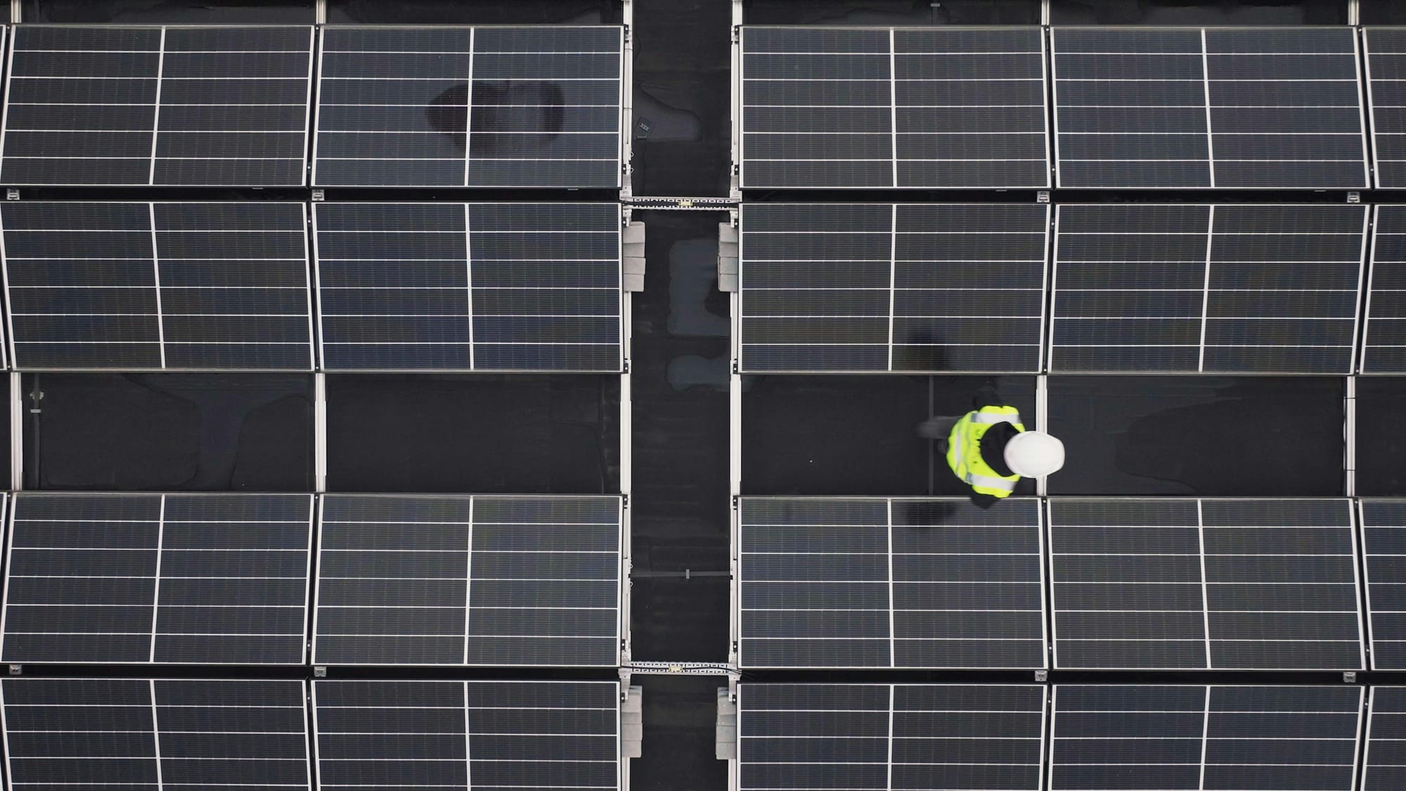 Aerial view of a worker in hi-vis safety gear inspecting solar panels.