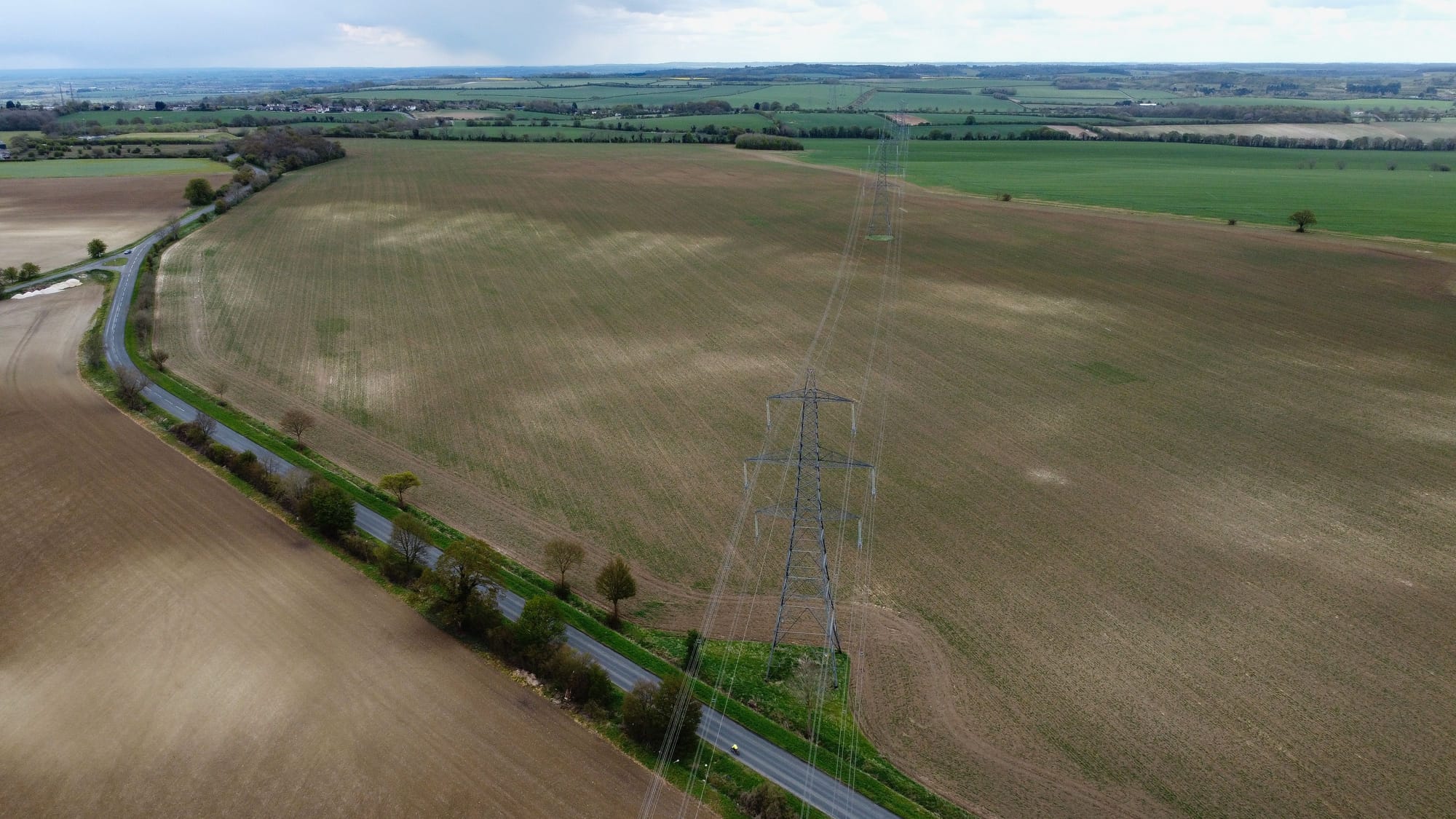 Aerial view of farmland with power transmission towers and lines crossing the fields in Central Bedfordshire, England.