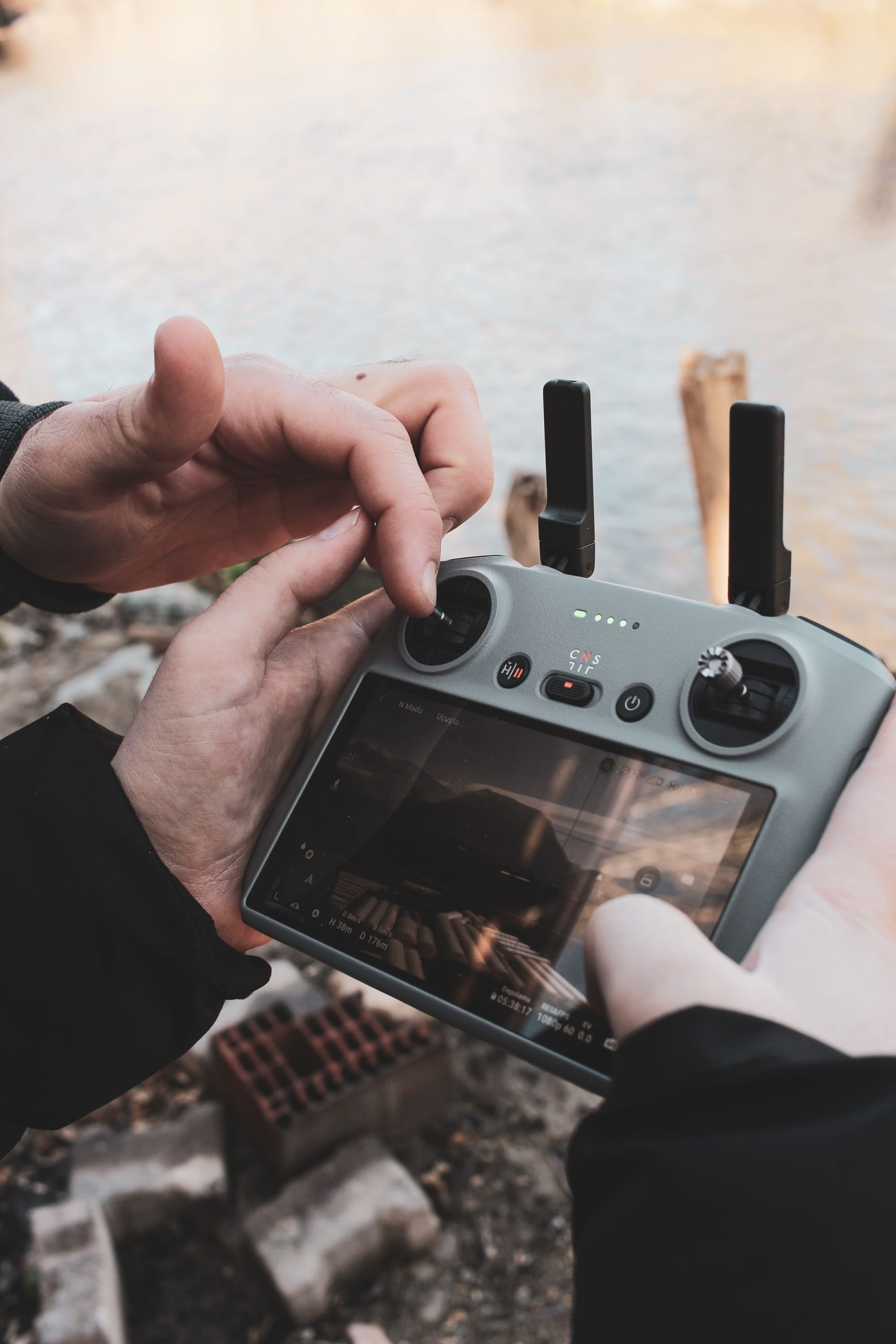 Close view of hands operating a drone controller with a live flight screen outdoors.