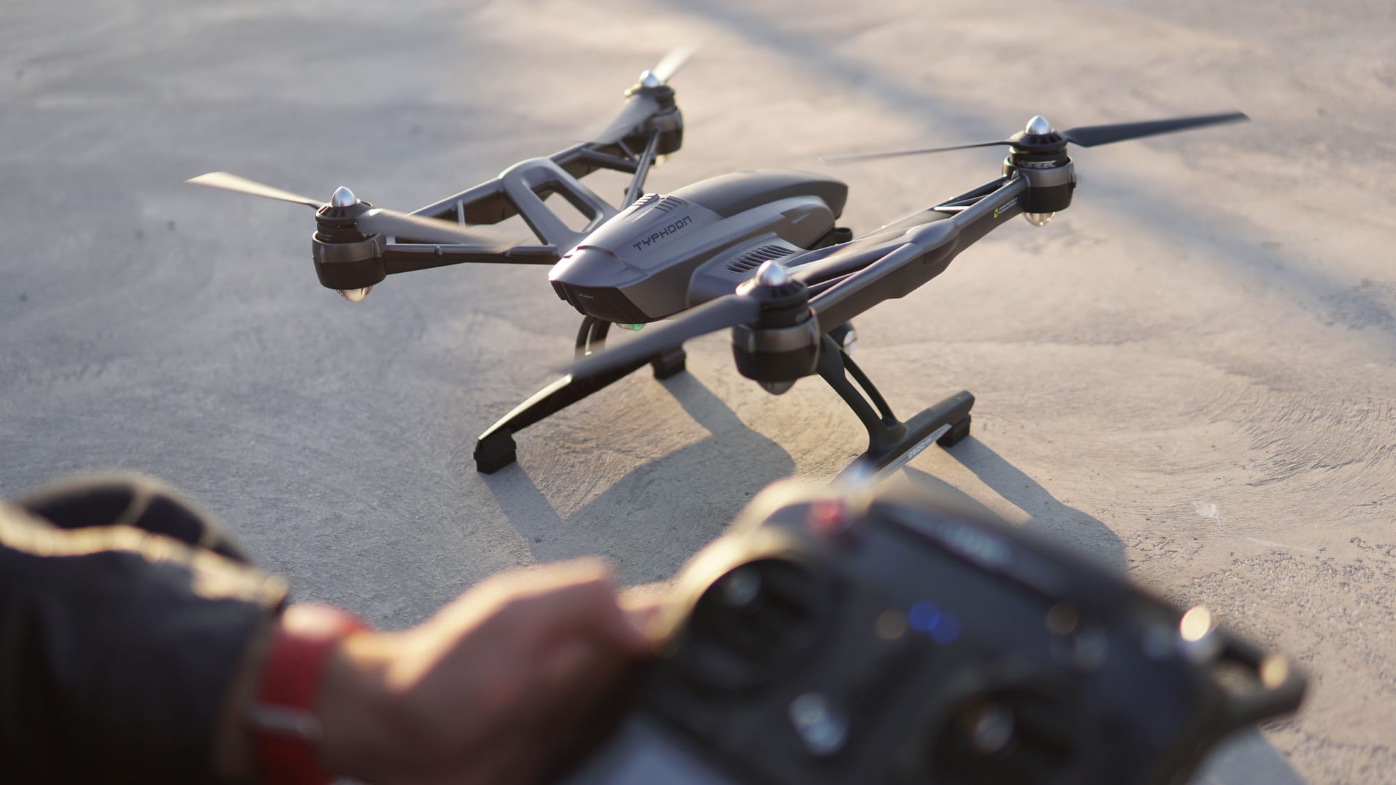 Top-down view of a quadcopter on pavement beside a drone operator holding a remote controller.