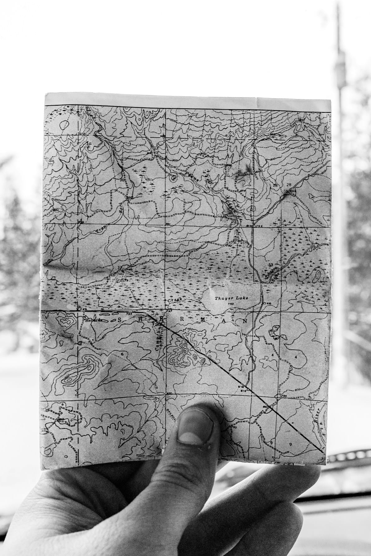 A hand holds a folded paper map showing contour lines and a lake.